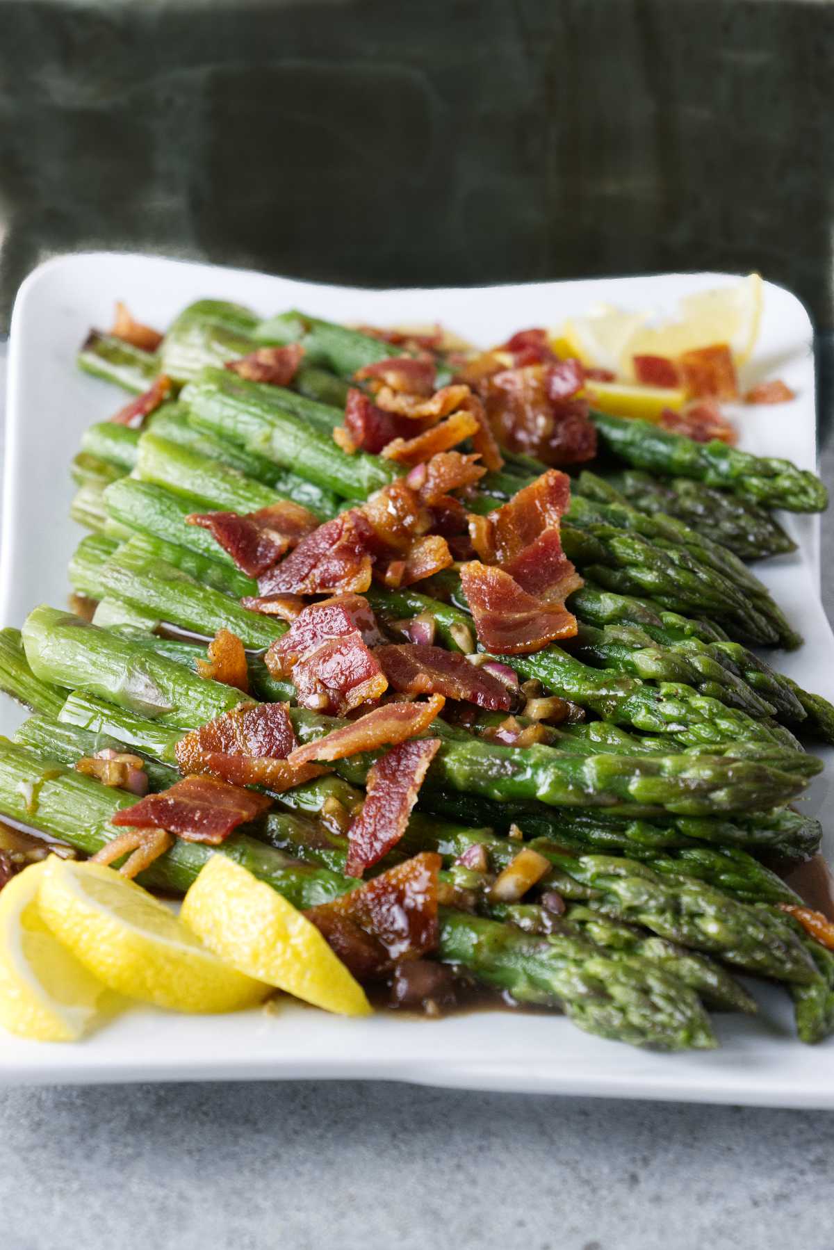 Asparagus cooked and plated with crumbled bacon, vinaigrette, and lemon wedges.