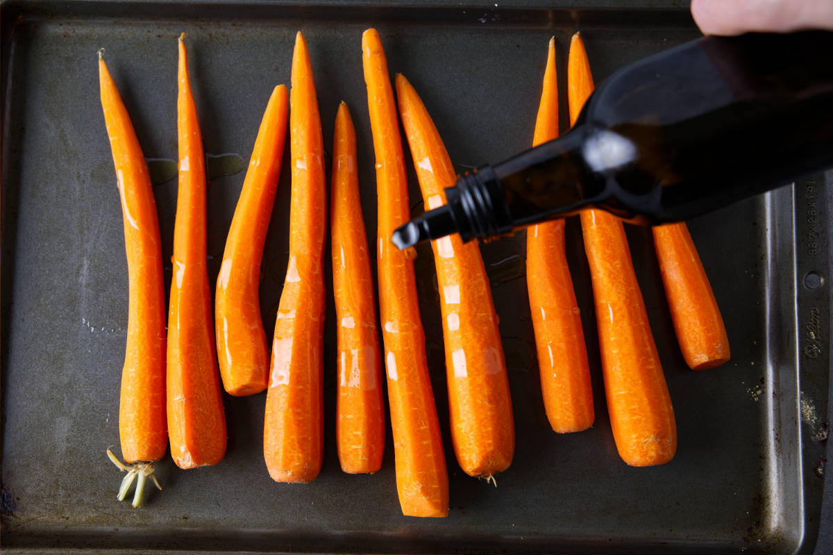 Drizzling olive oil over carrots in a sheet pan.