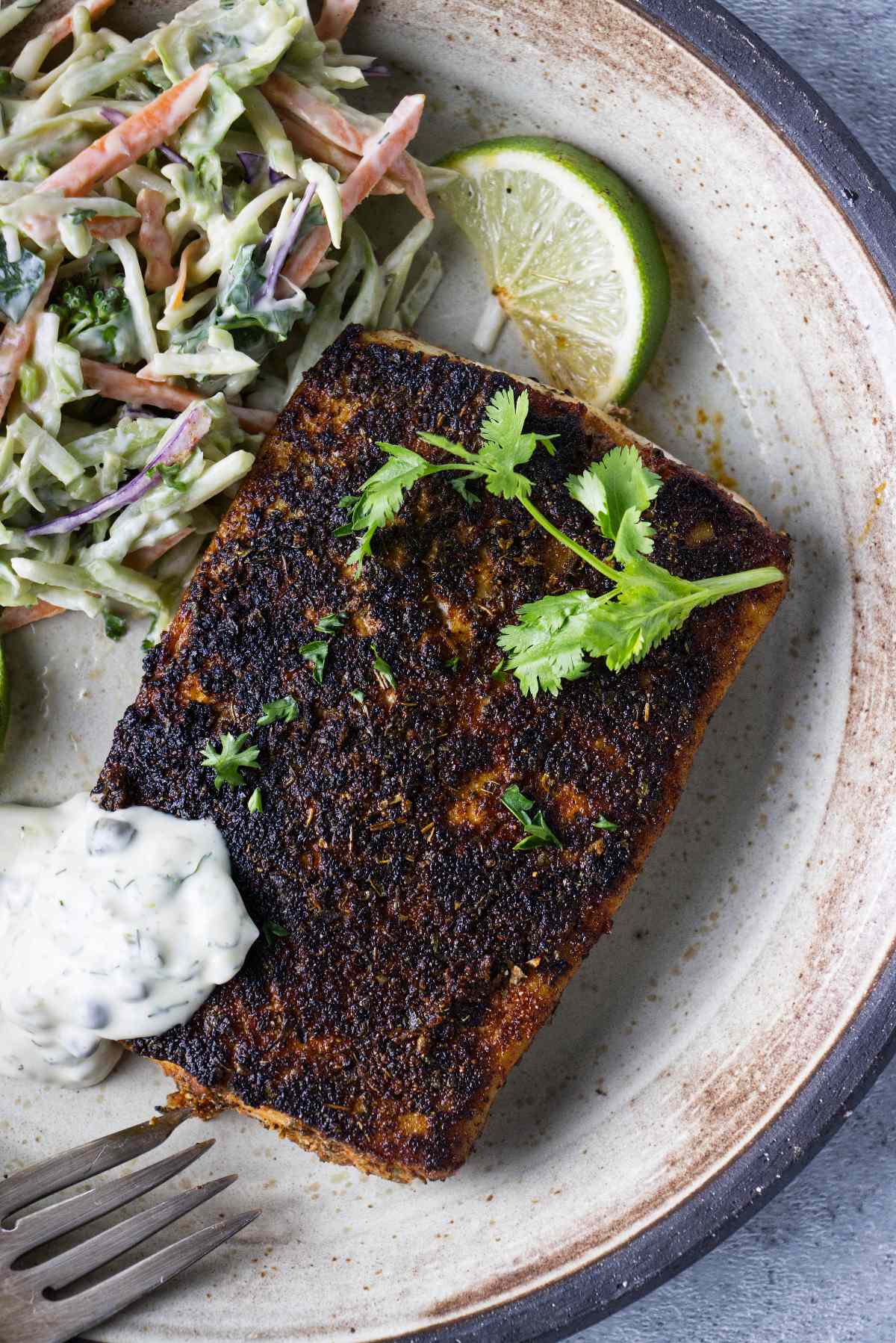 Blackened mahi mahi on plate with coleslaw and dill caper sauce.