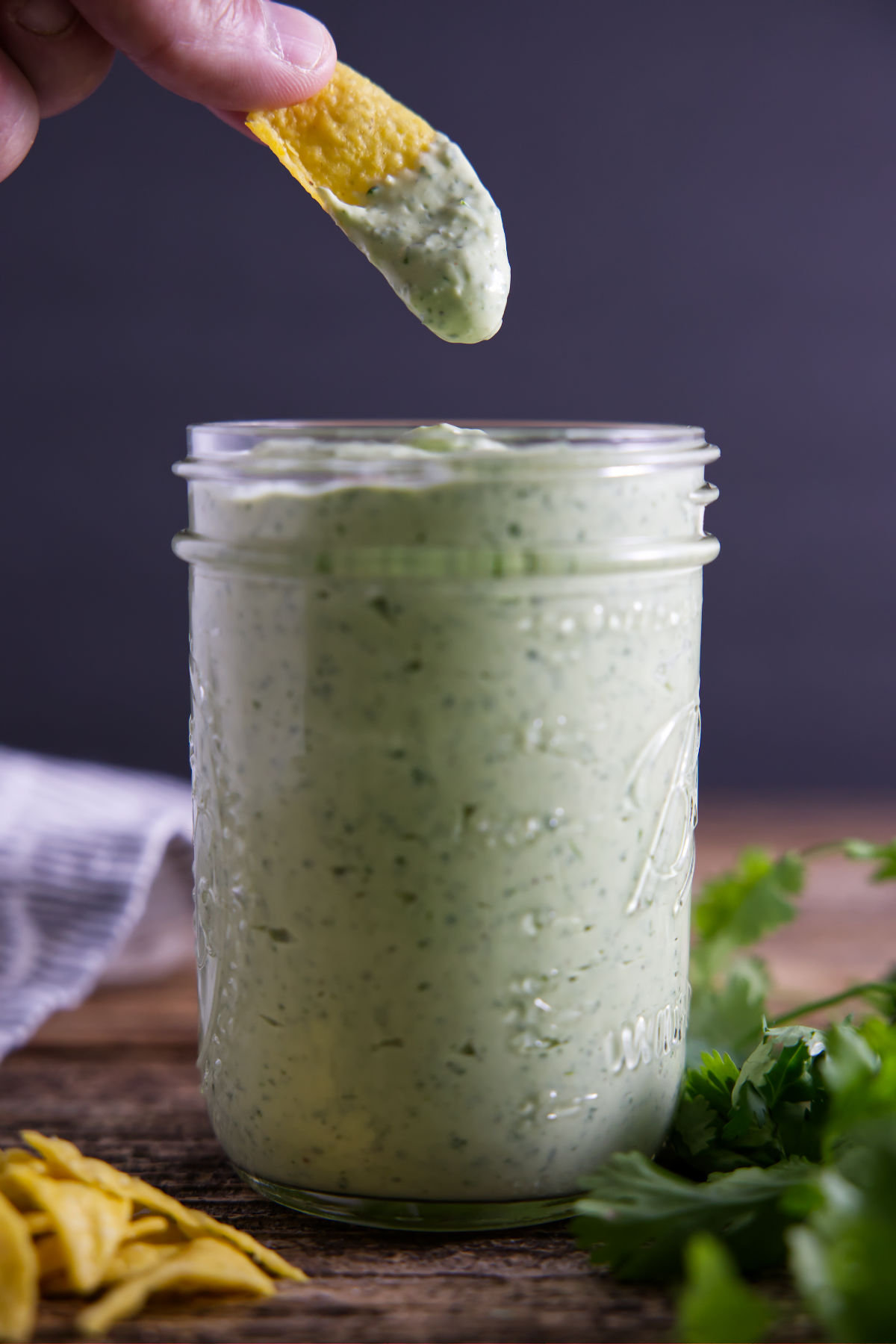 Chip being dipped into avocado lime crema sauce stored in a mason jar.