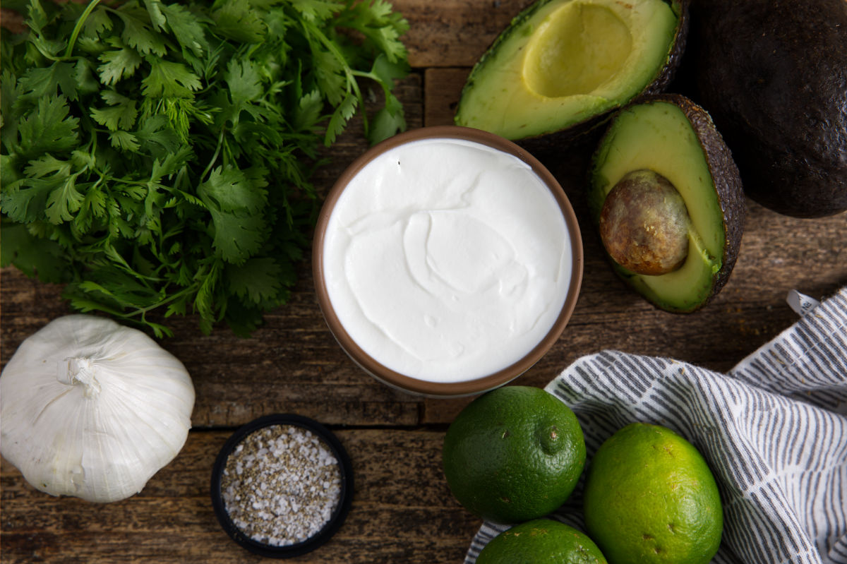 Ingredients for avocado lime crema including sour cream, avocados, lime, and herbs and seasoning.