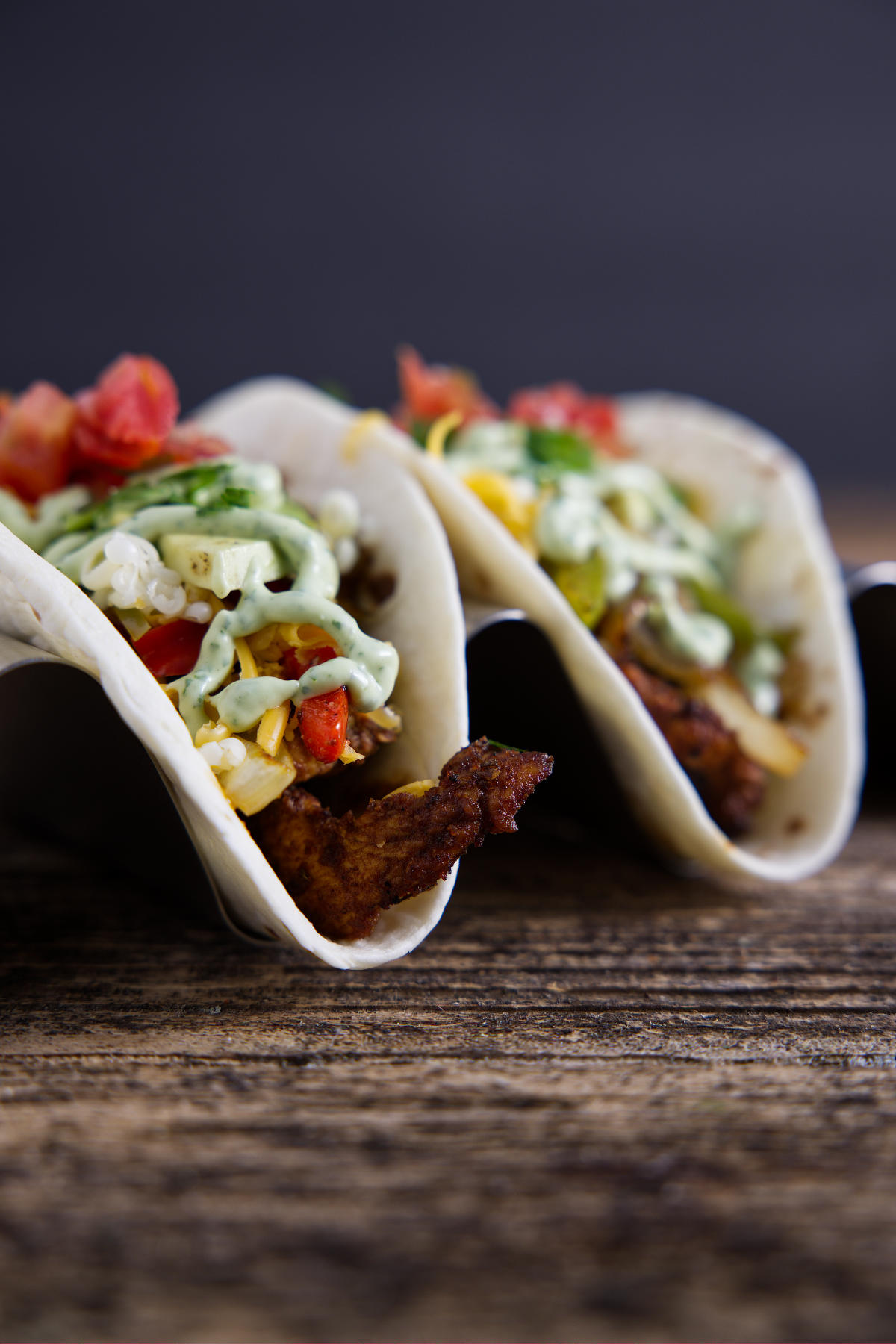 Two tacos filled with Blackstone fajita fixings and topped with a drizzle of avocado crema.