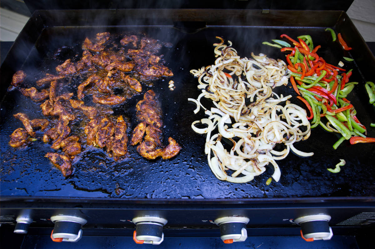 Cooking fajitas on the Blackstone griddle, with chicken, onions, and bell peppers in separate piles.