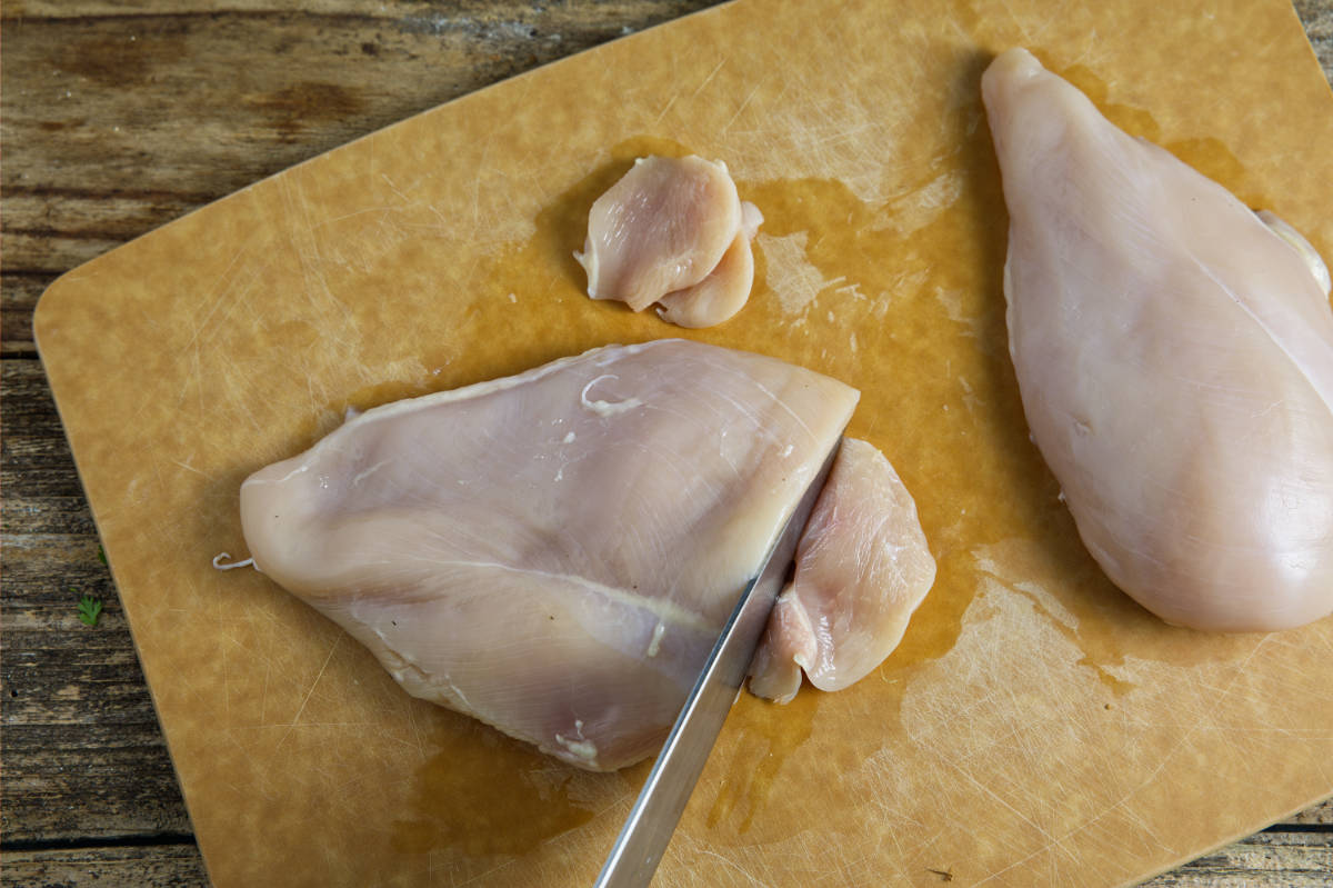 Slicing chicken breast on cutting board.