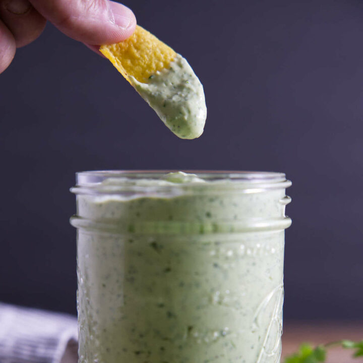 Avocado lime crema sauce with chip dipping into the jar.