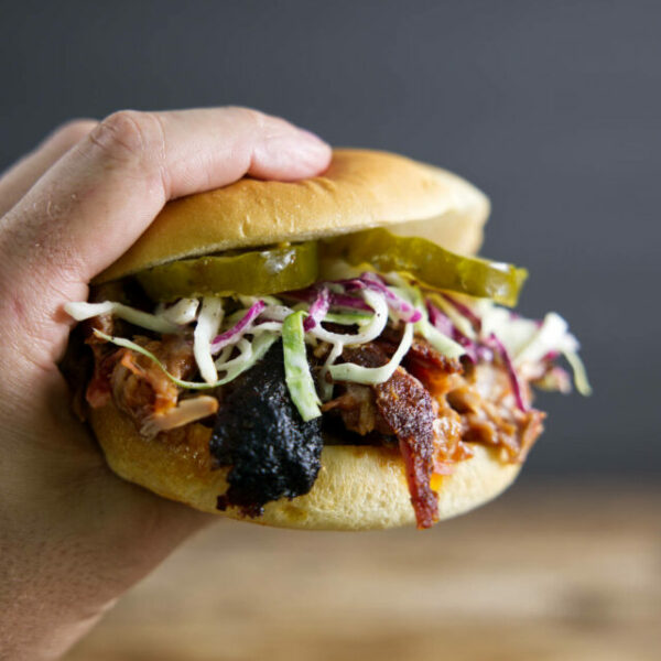 Pulled pork sandwich made from smoked pork butt (smoked pork shoulder). With pickles, slaw, and BBQ sauce.