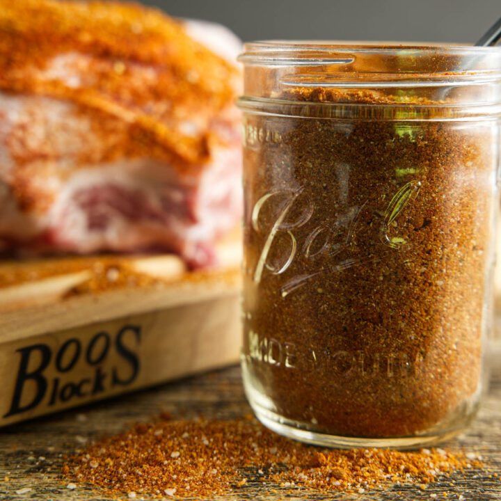 jar of pork butt rub with a seasoned pork butt in the background