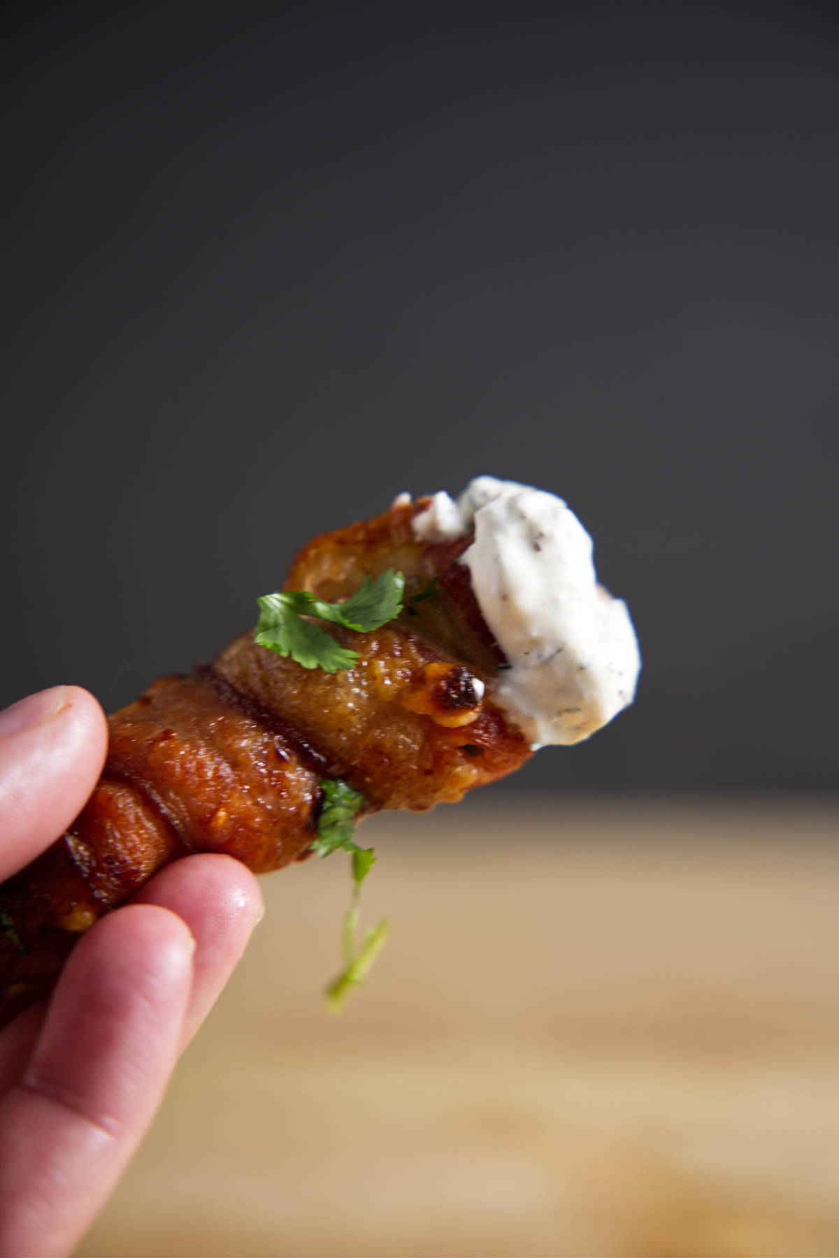 Single bacon wrapped jalapeño popper dipped in blue cheese dressing held in hand.