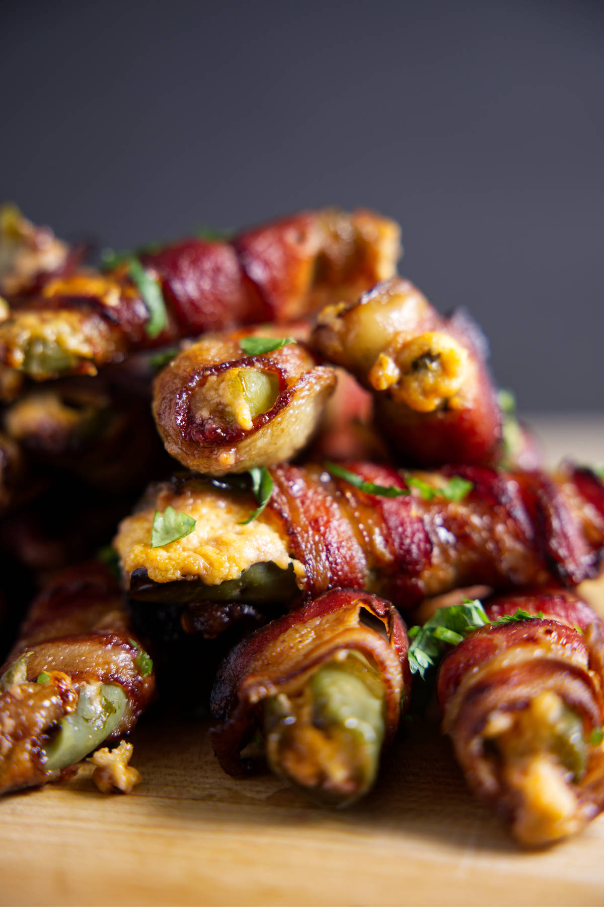 Large pile of bacon wrapped jalapeño poppers with cheese oozing out.