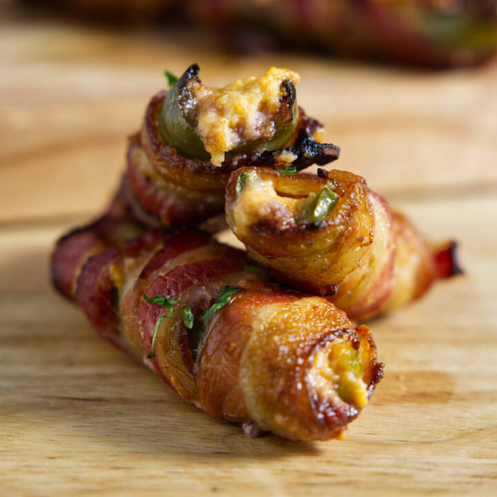 Stacked jalapeño poppers on a cutting board, and these are wrapped in cripsy bacon!
