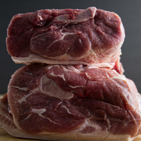 Pork shoulder (picnic shoulder) and pork butt (Boston butt) stacked on a butcher block.