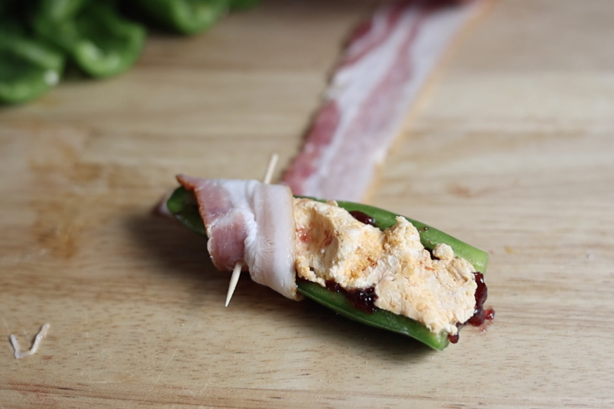Wrapping stuffed jalapeno in a slice of bacon.