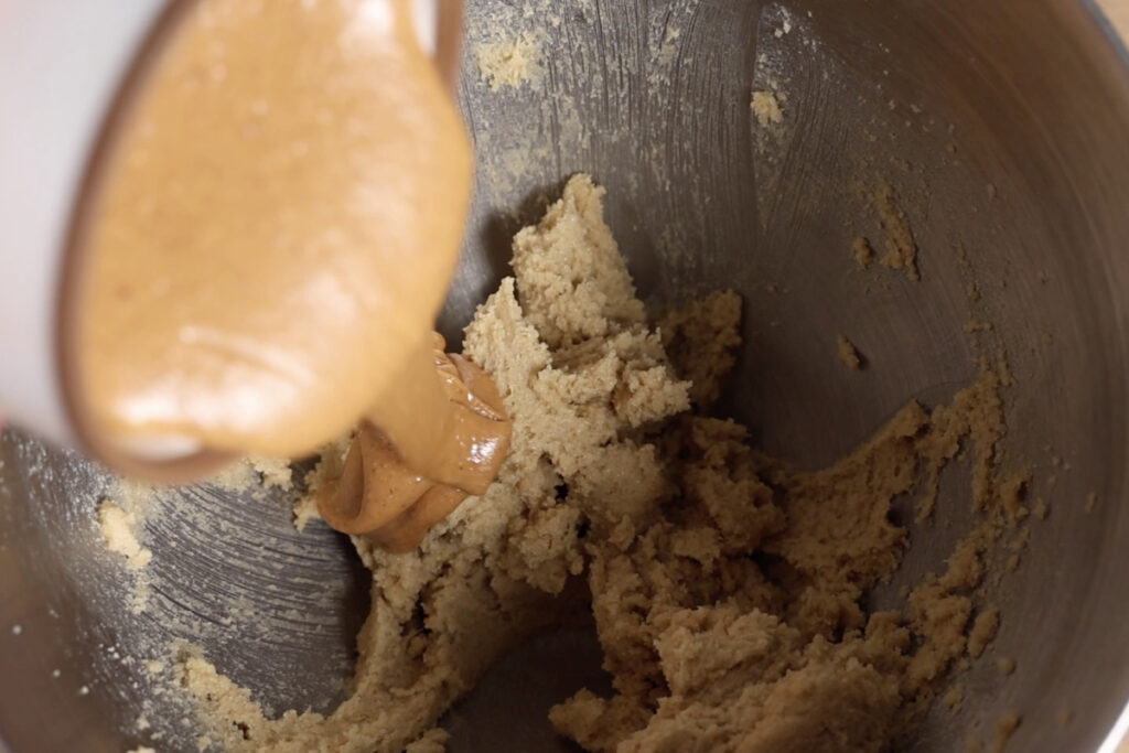 Adding peanut butter to cookie dough in mixing bowl.