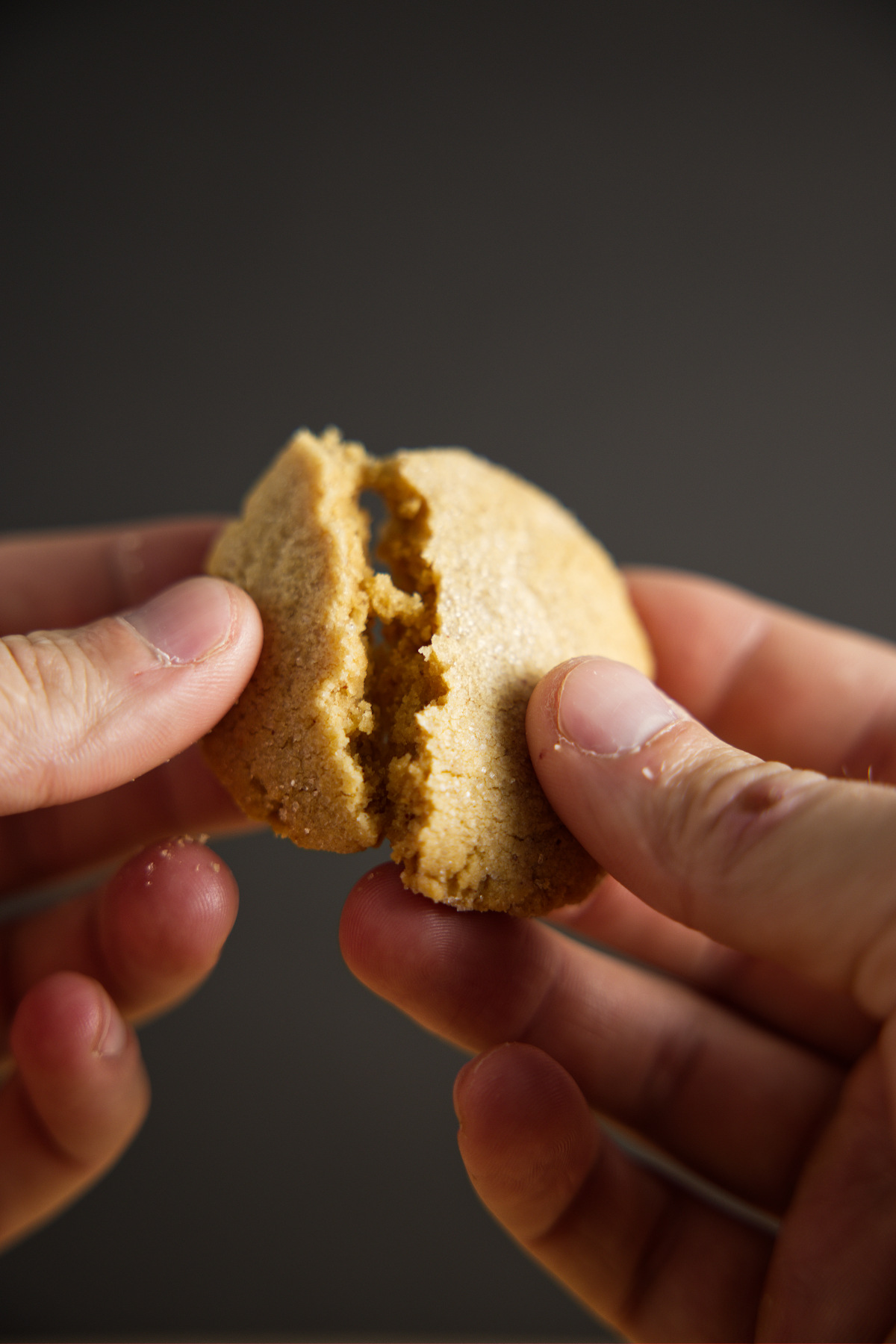 Holding a peanut better cookie and breaking it in half.