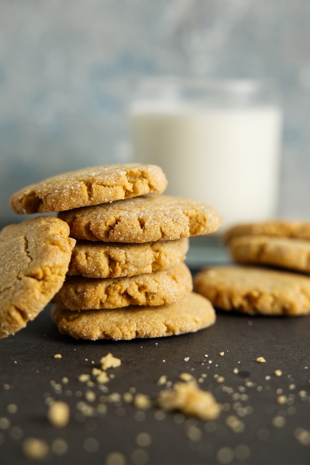 Several peanut butter cookies stacked in a pile with crumbs scattered around and a glass of milk.