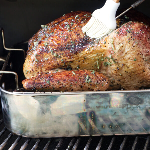 Basting the turkey while it smokes on the Traeger pellet grill.