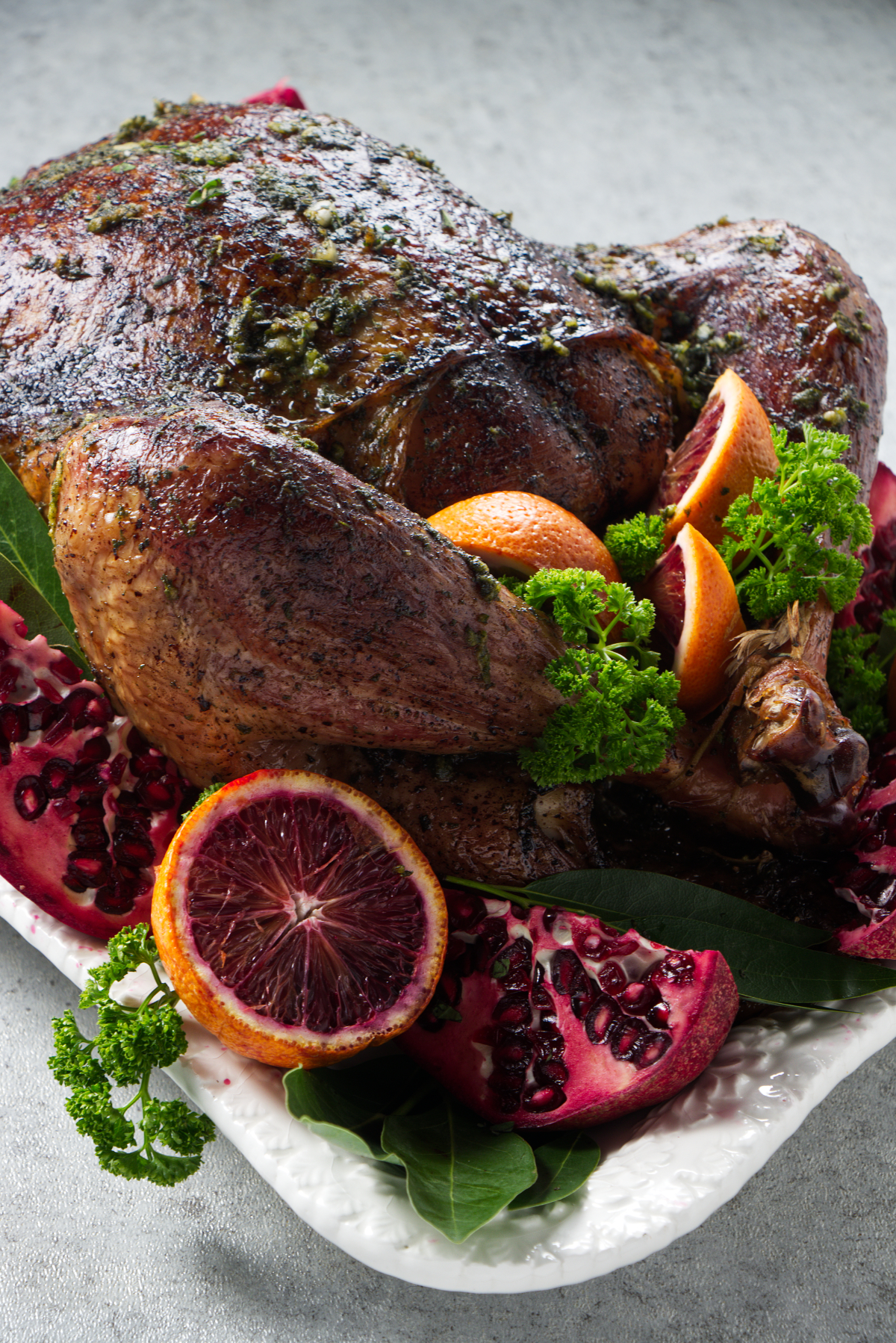 Whole dry brine smoked turkey on a platter arranged with citrus, pomegranate, and herbs as garnish.