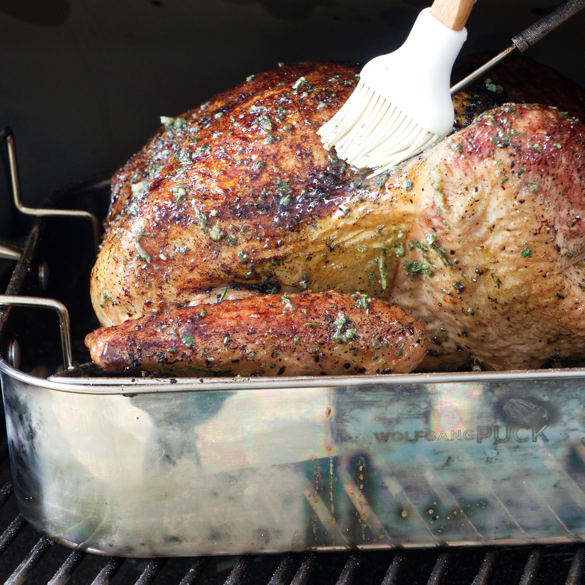 Basting the smoked turkey while it is on the pellet smoker grill.