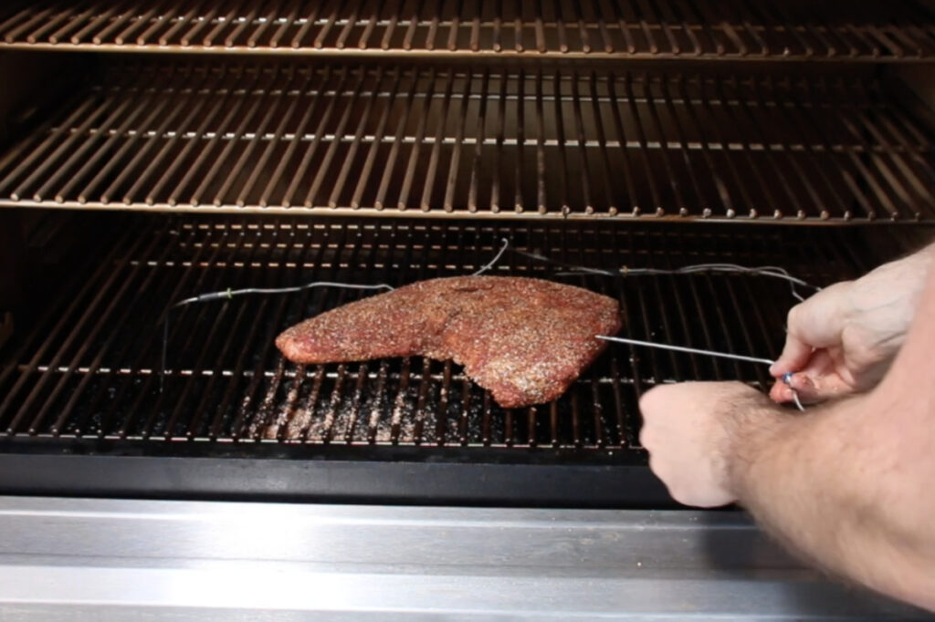 Seasoned tri-tip on Traeger smoker, putting thermometer probe into meat.