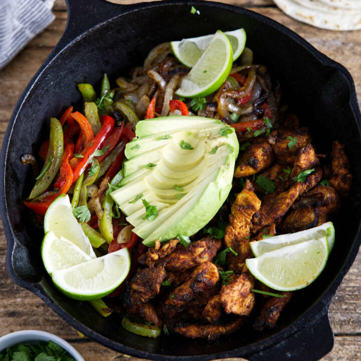 Fajitas in cast iron skillet with avocado and lime slices.