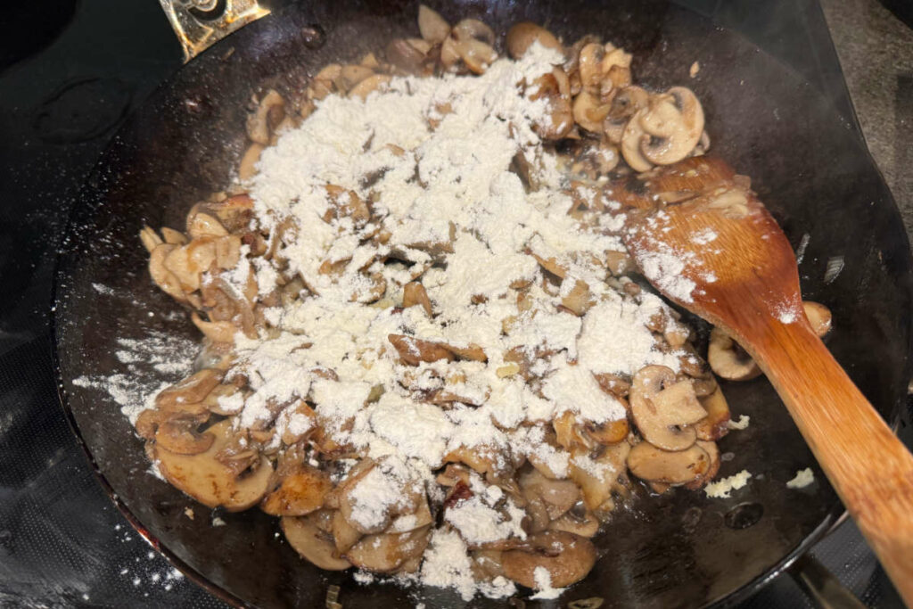 Adding flour to cooked mushrooms in the frying pan.