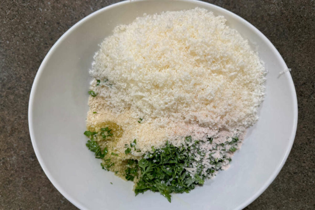 Combining cheese, herbs, oil, and seasoning to bread crumbs for the casserole topping.