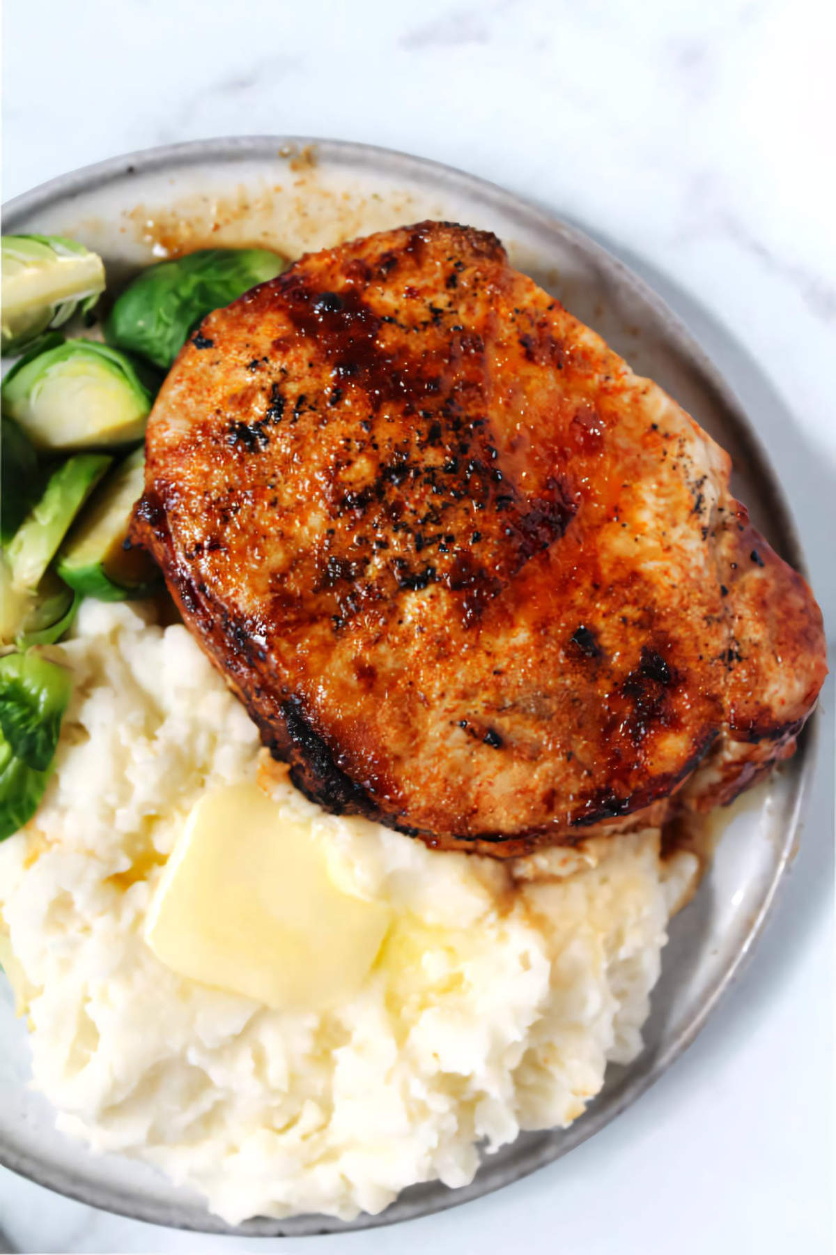 Chipotle crusted pork chop plated with mashed potatoes and Brussels sprouts.