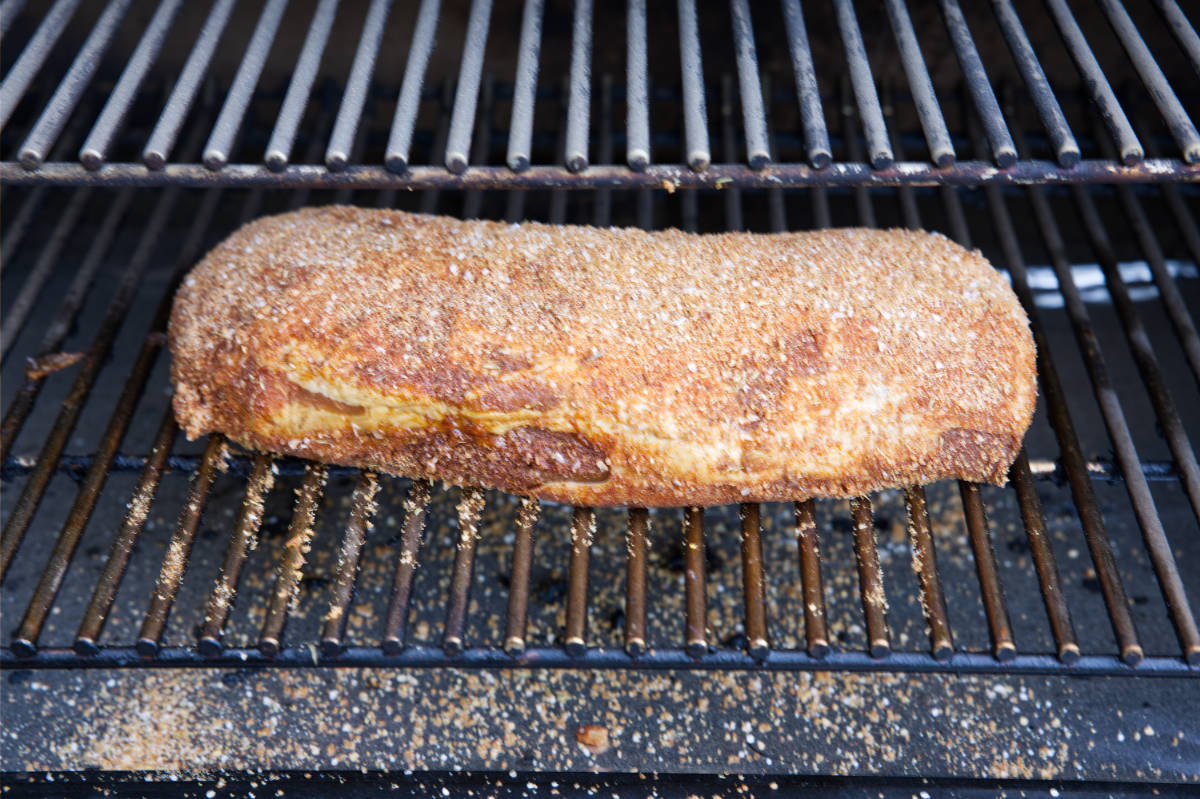 Pork loin with dry rub on grill grates of smoker.