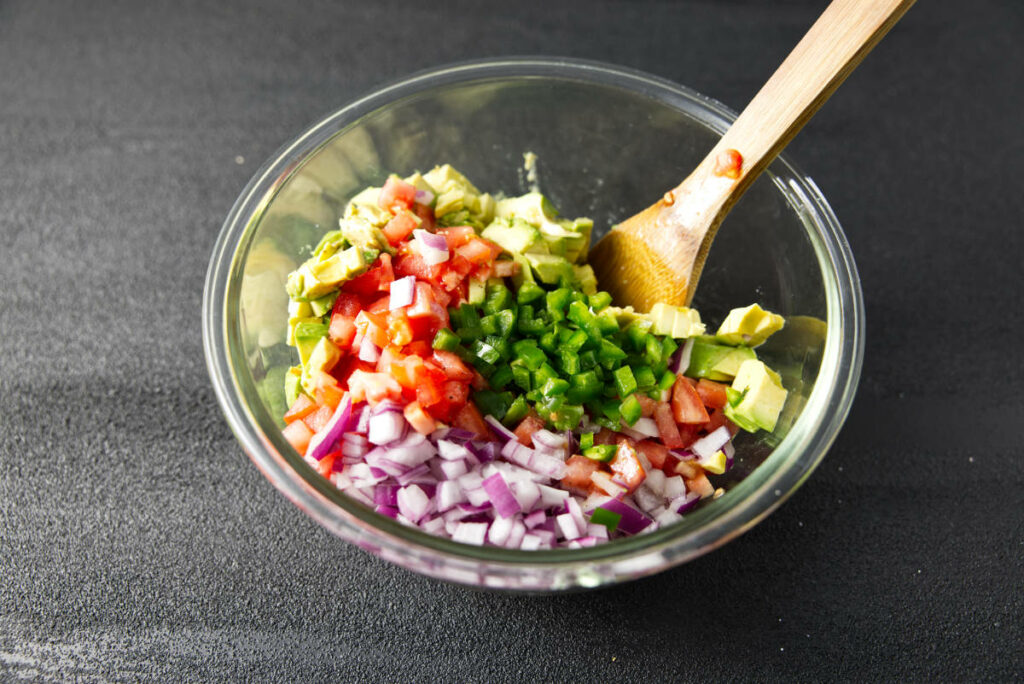 Combining the ingredients for the avocado salsa in a large glass bowl.