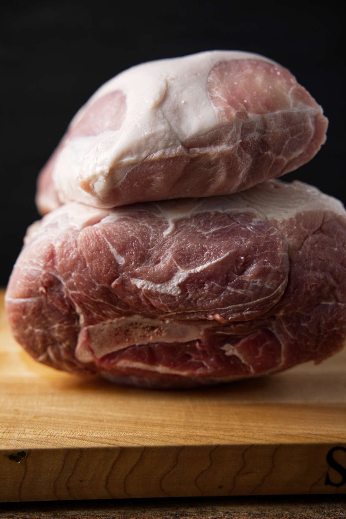 Pork loin on top of a pork shoulder sitting on a butcher block.