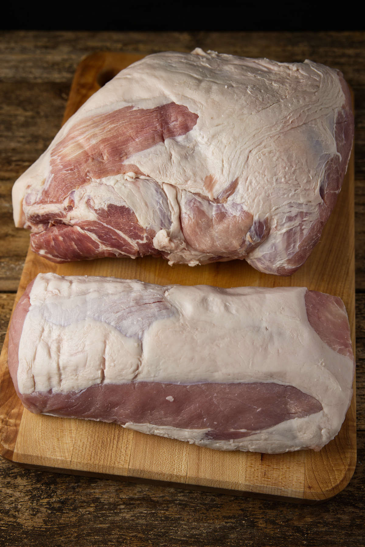 Pork shoulder vs pork loin side-by-side laying on a butcher block.