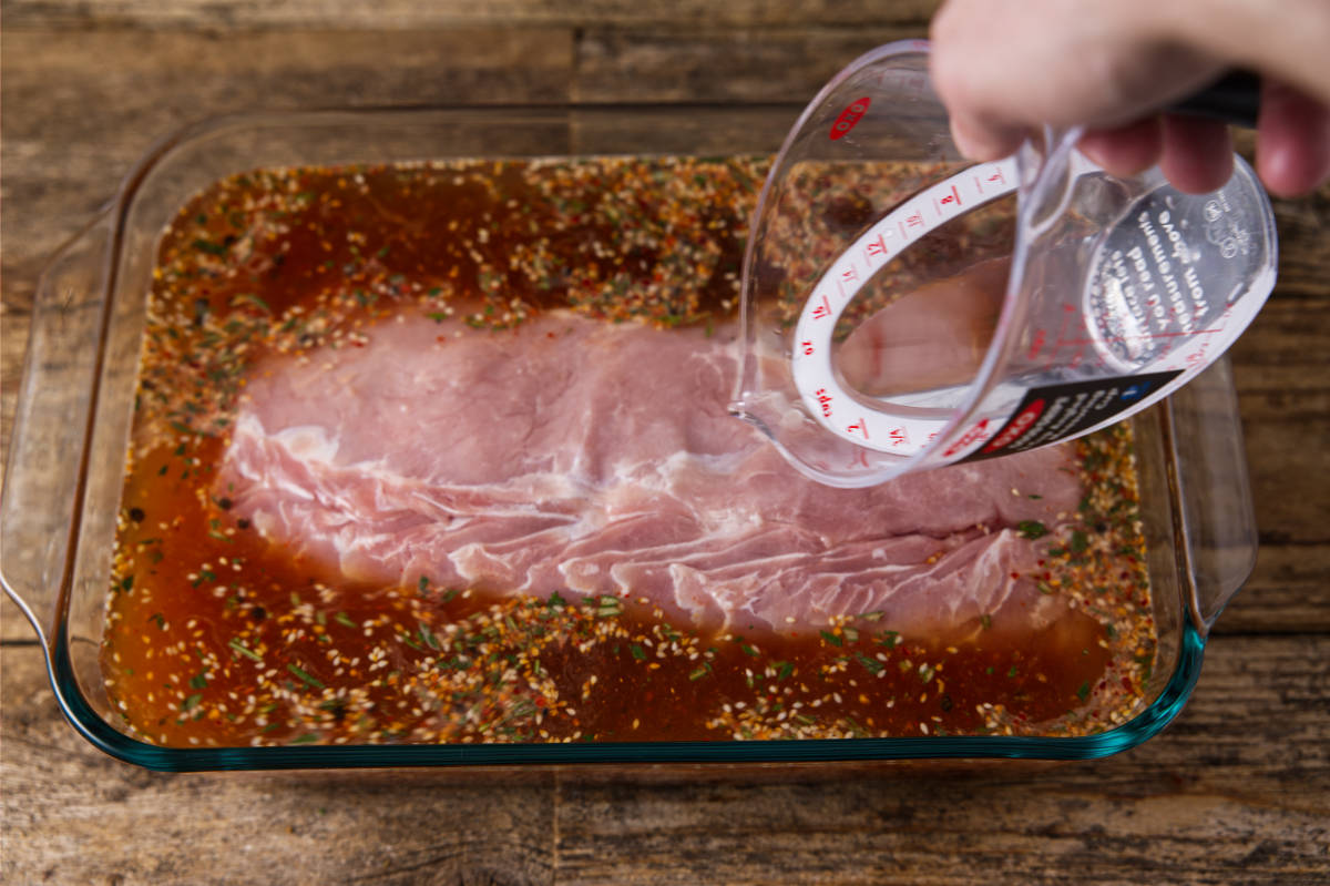 Pouring water over pork loin resting in brine in bowl.