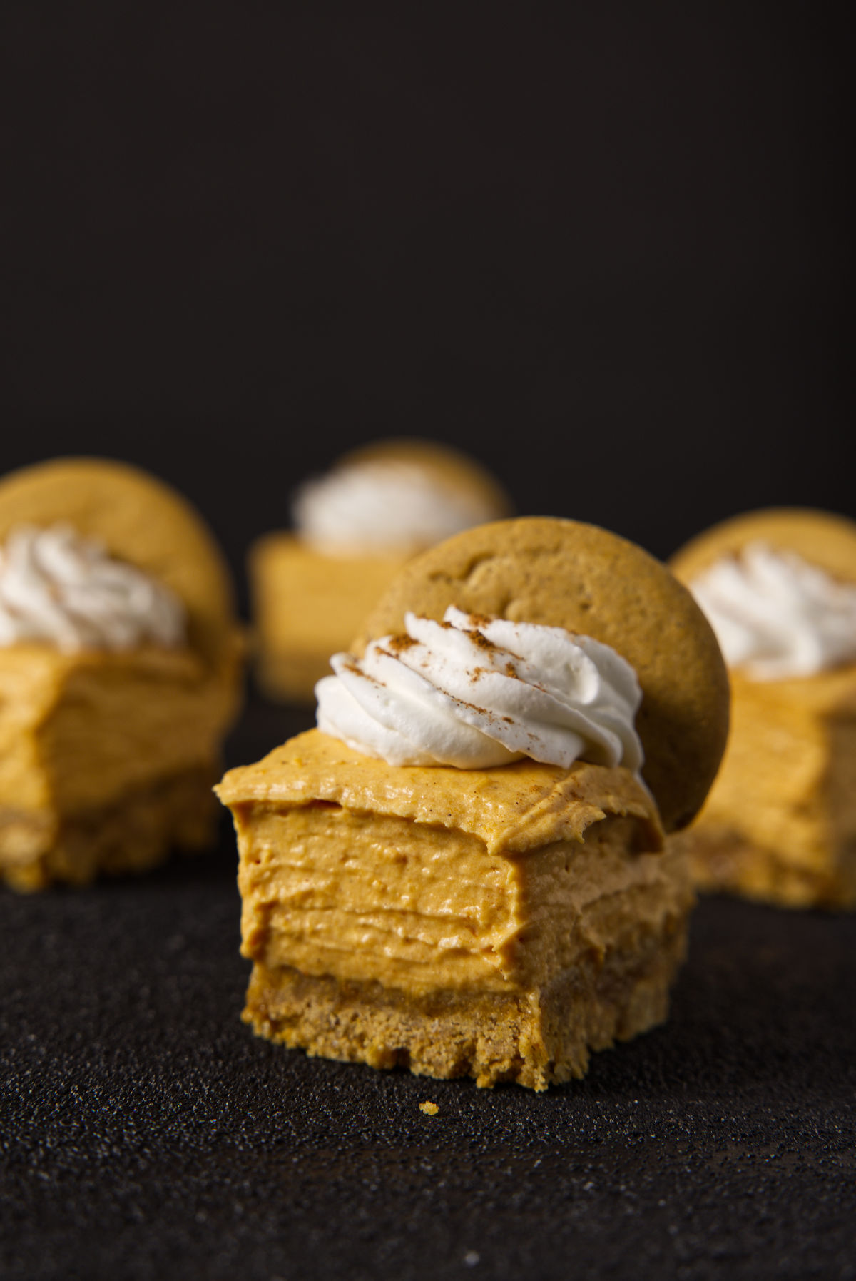 Very close up shot of no bake pumpkin cheesecake bars on a charcoal black surface.