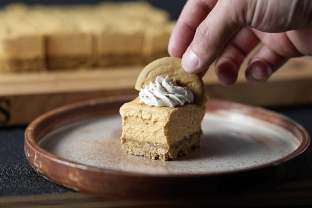 Topping the no bake pumpkin cheesecake bars with whipped cream and a gingersnap cookie.