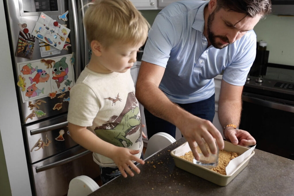 Using a glass to press cookie crumb crust into a square pan.