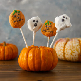 Pumpkin and ghost cake pops, decorated and proped up in a pumpkin decoration.