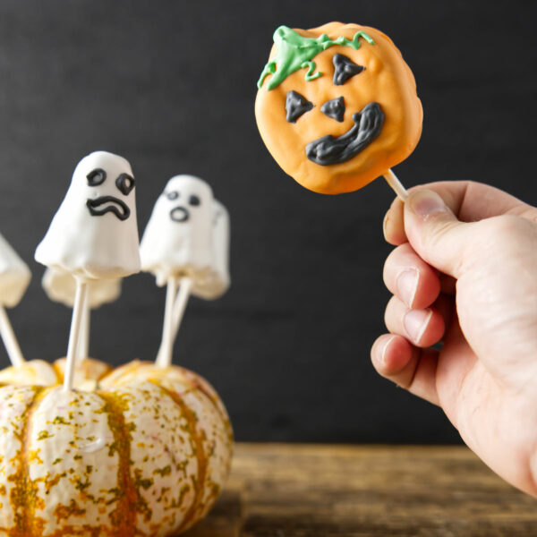 Jack-o'-lantern and ghost cake pops sticking out of pumpkin.