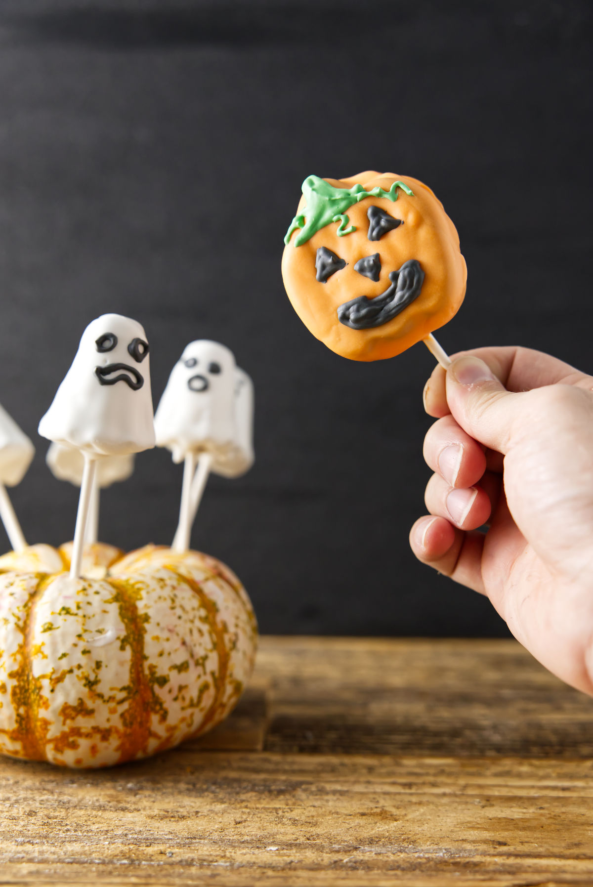 Jack-o'-lantern and ghost cake pops sticking out of pumpkin.