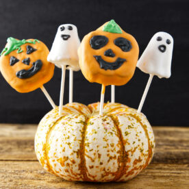 Jack-o'-lantern and ghost cake pops sticking out of pumpkin.