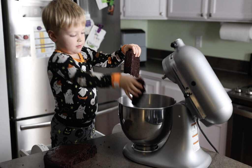 Breaking up a chocolate cake and adding it to a stand mixer.