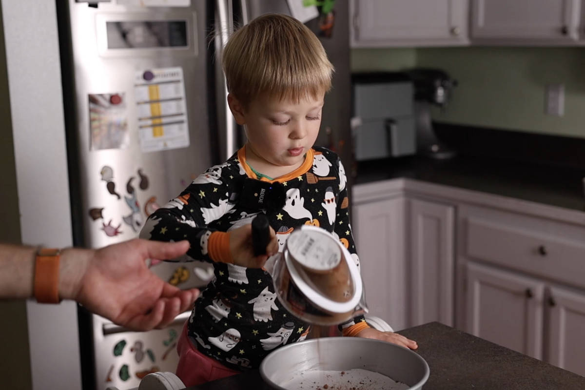 Preparing cake pan with grease, parchment paper, and cocoa powder.