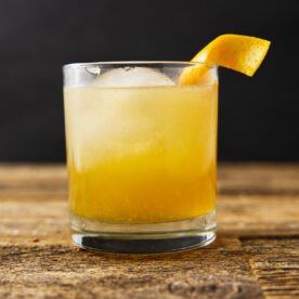 Close up of a maple bourbon smash with an orange peel twist hanging on the rim.