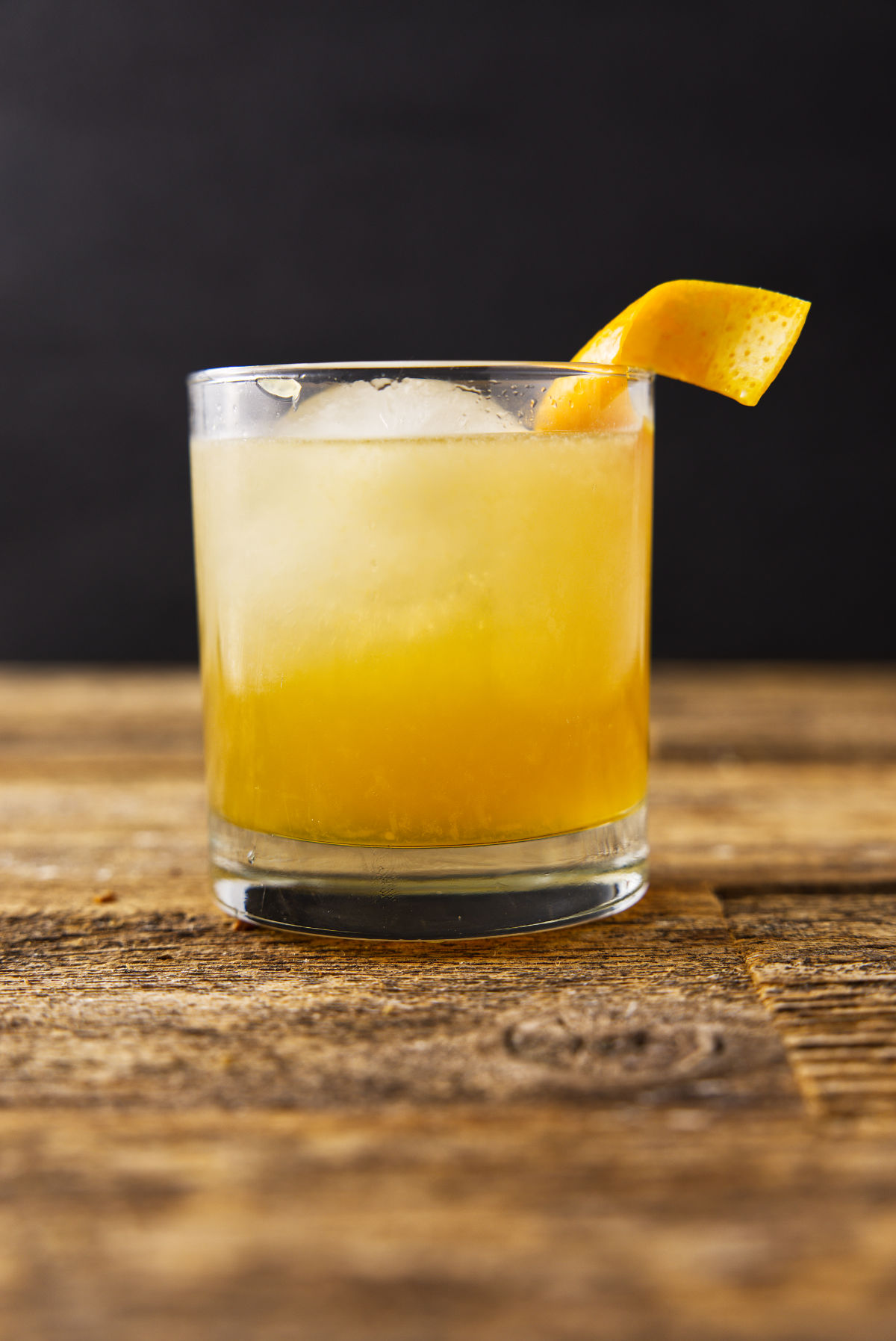 Glass filled with maple bourbon smash with an orange peel twist hanging on the rim of the glass.