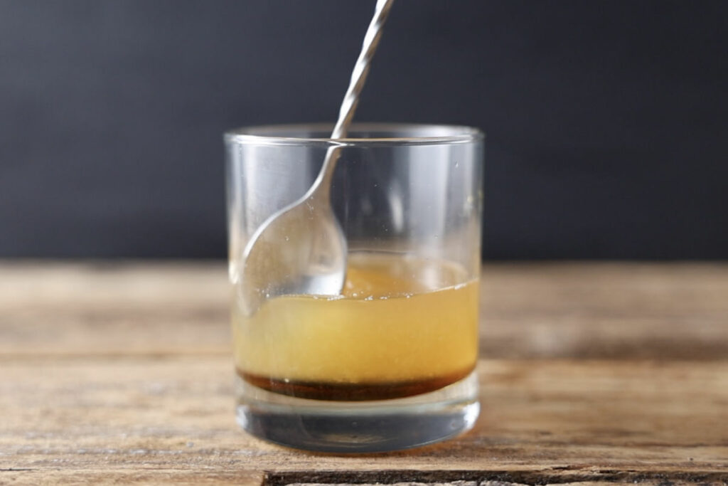 Stirring maple bourbon smash in glass.