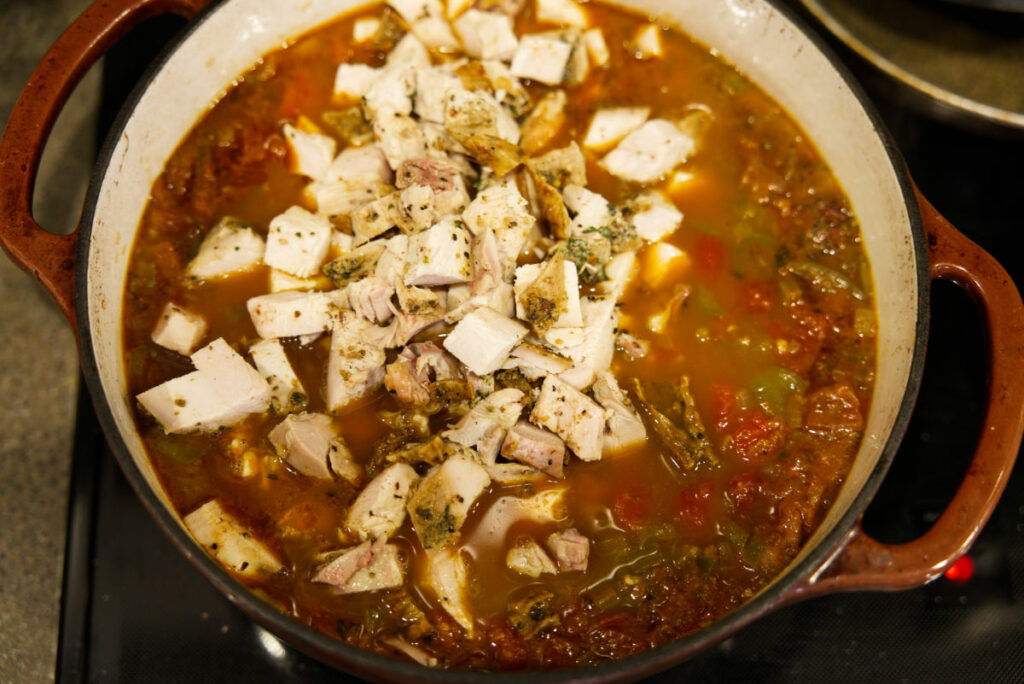 Adding leftover turkey to the chili in a Dutch oven.