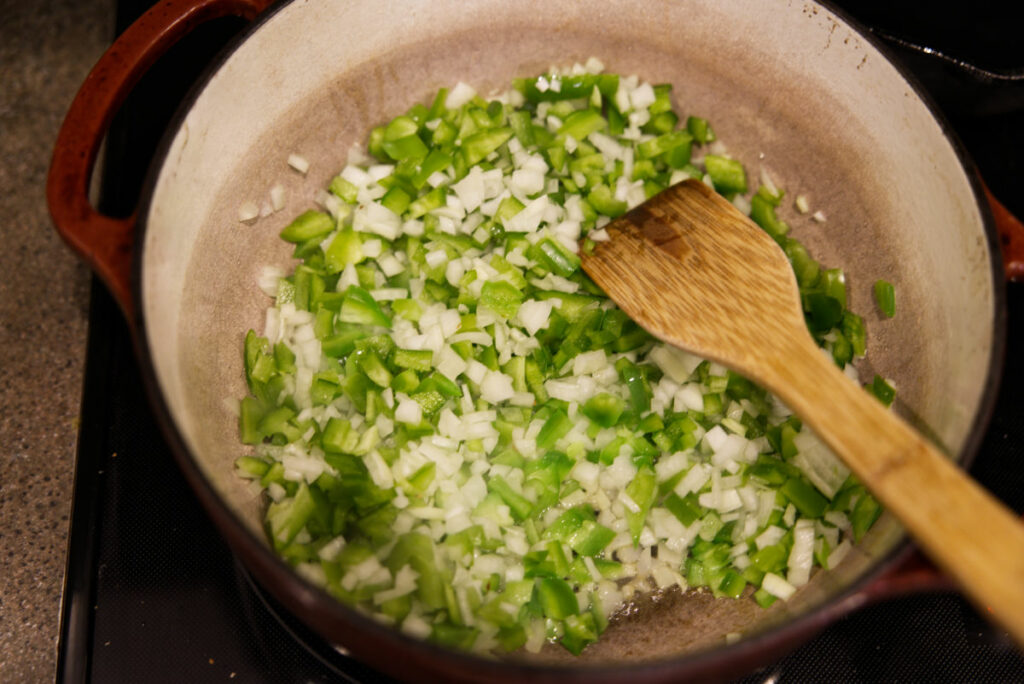 Sauteing onions and green bell pepper in a Dutch oven.