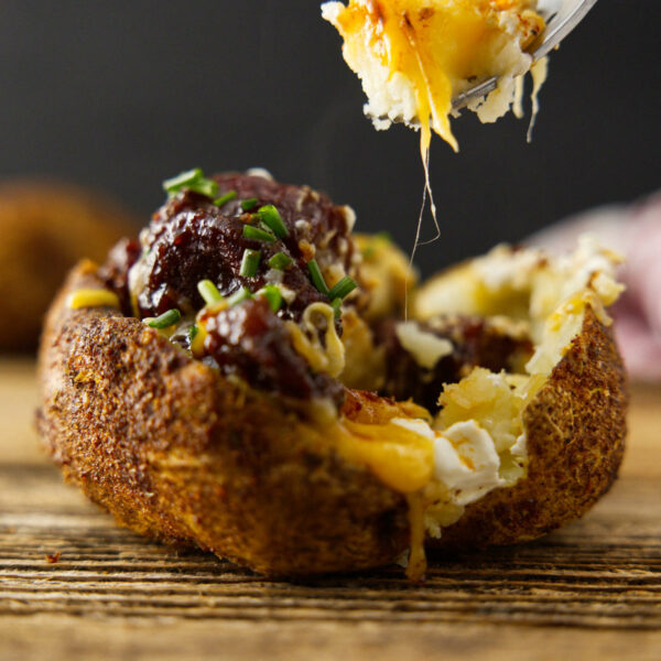 Fully loaded baked potato with a fork loaded with potato and melty cheese.