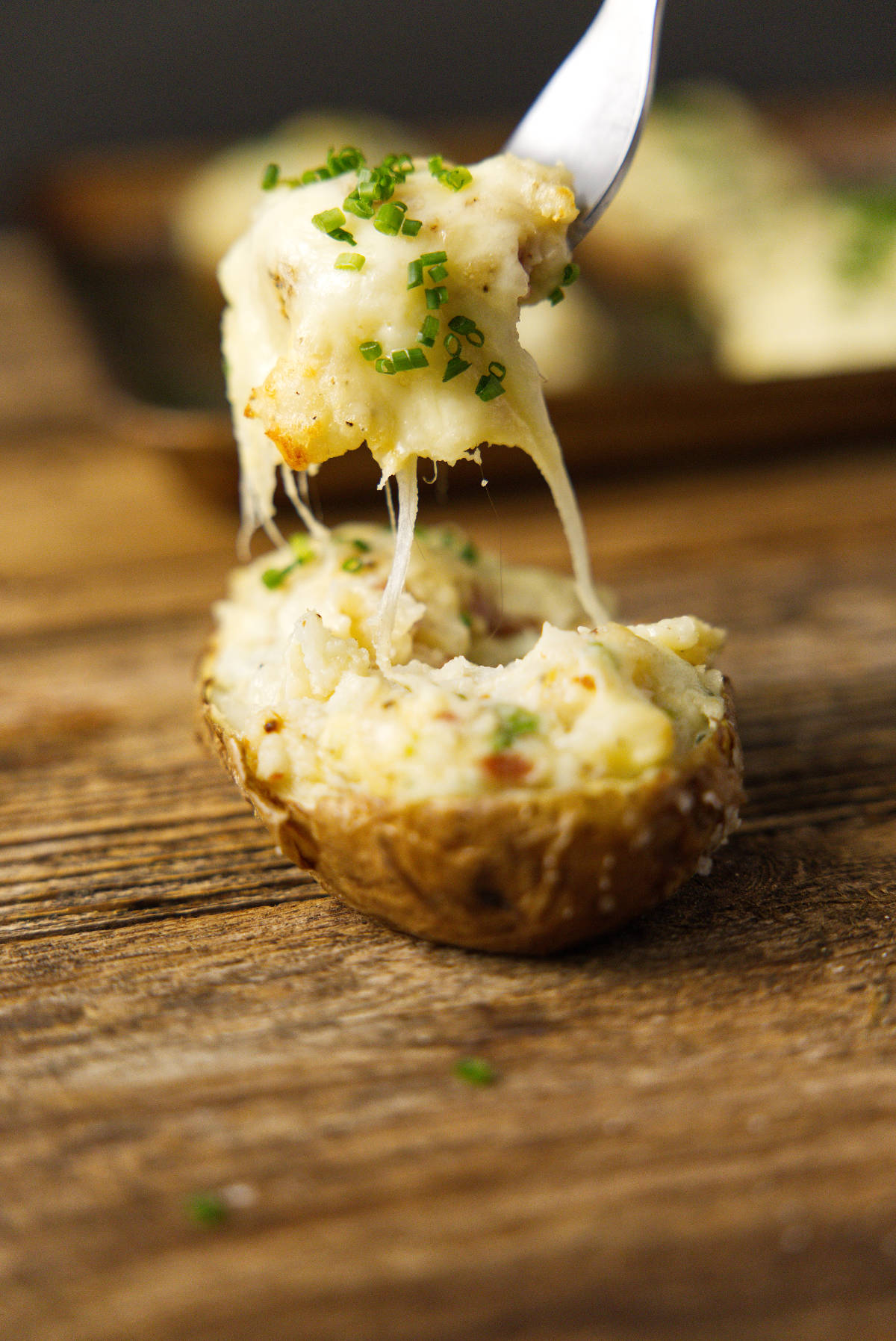 Fork scooping a bite of smoked twice baked potato with a gooey cheese pull.