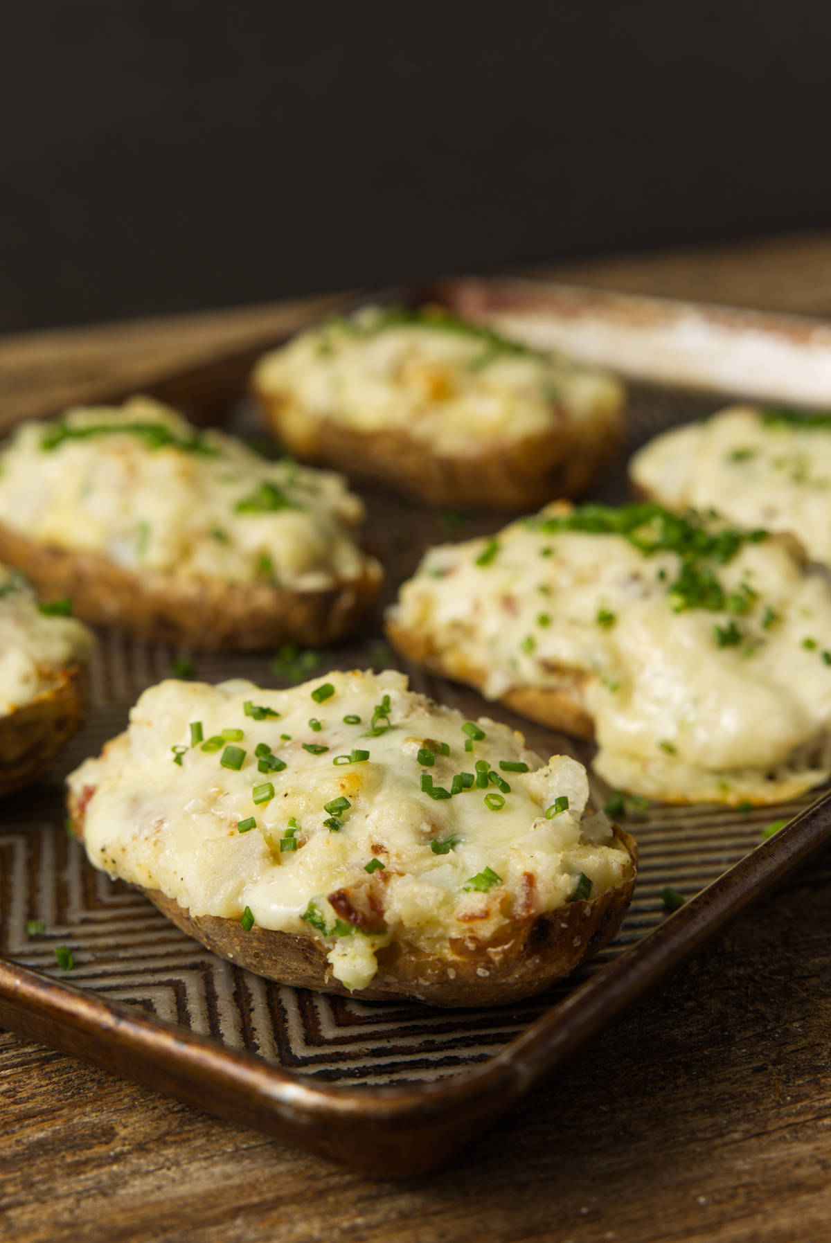 Smoked twice baked potatoes with gooey cheese and topped with chives resting on a baking pan.