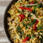 Close up of Elote Mexican street corn pasta salad, with vibrant red tortilla strips, charred corn, crispy bits of bacon, and a creamy dressing.